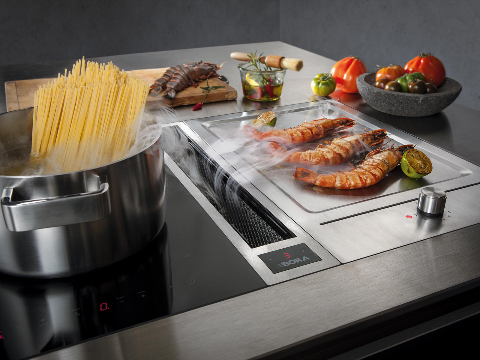 BORA kookplaat met teppanyaki en afzuiging, garnalen op de bakplaat naast een pan met spaghetti