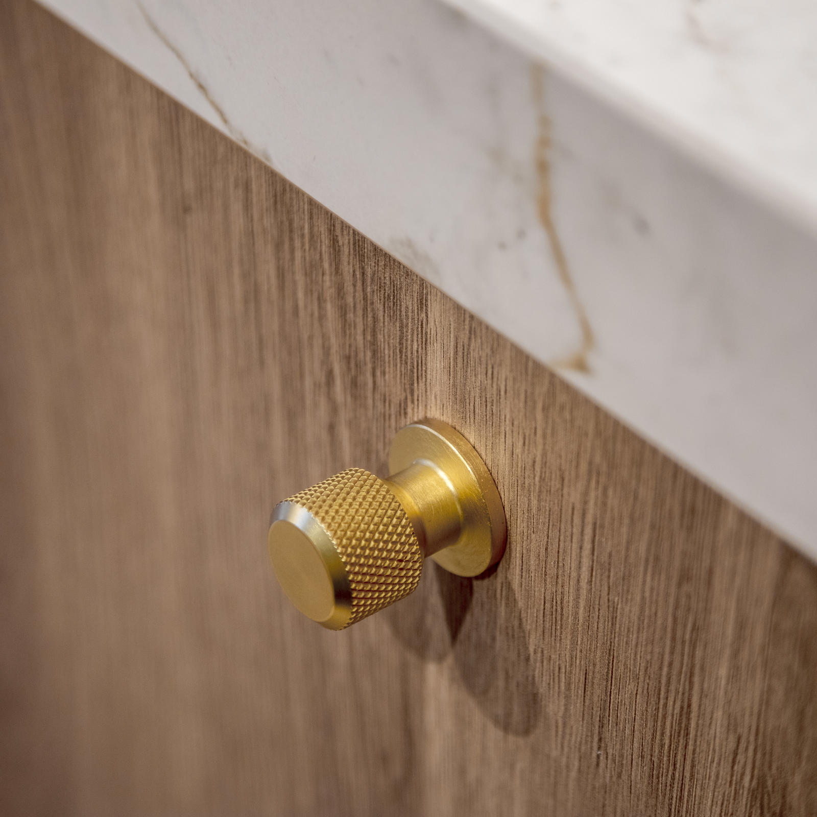 Goudkleurige gekartelde knop op houten keukenfront onder een gemarmerd werkblad