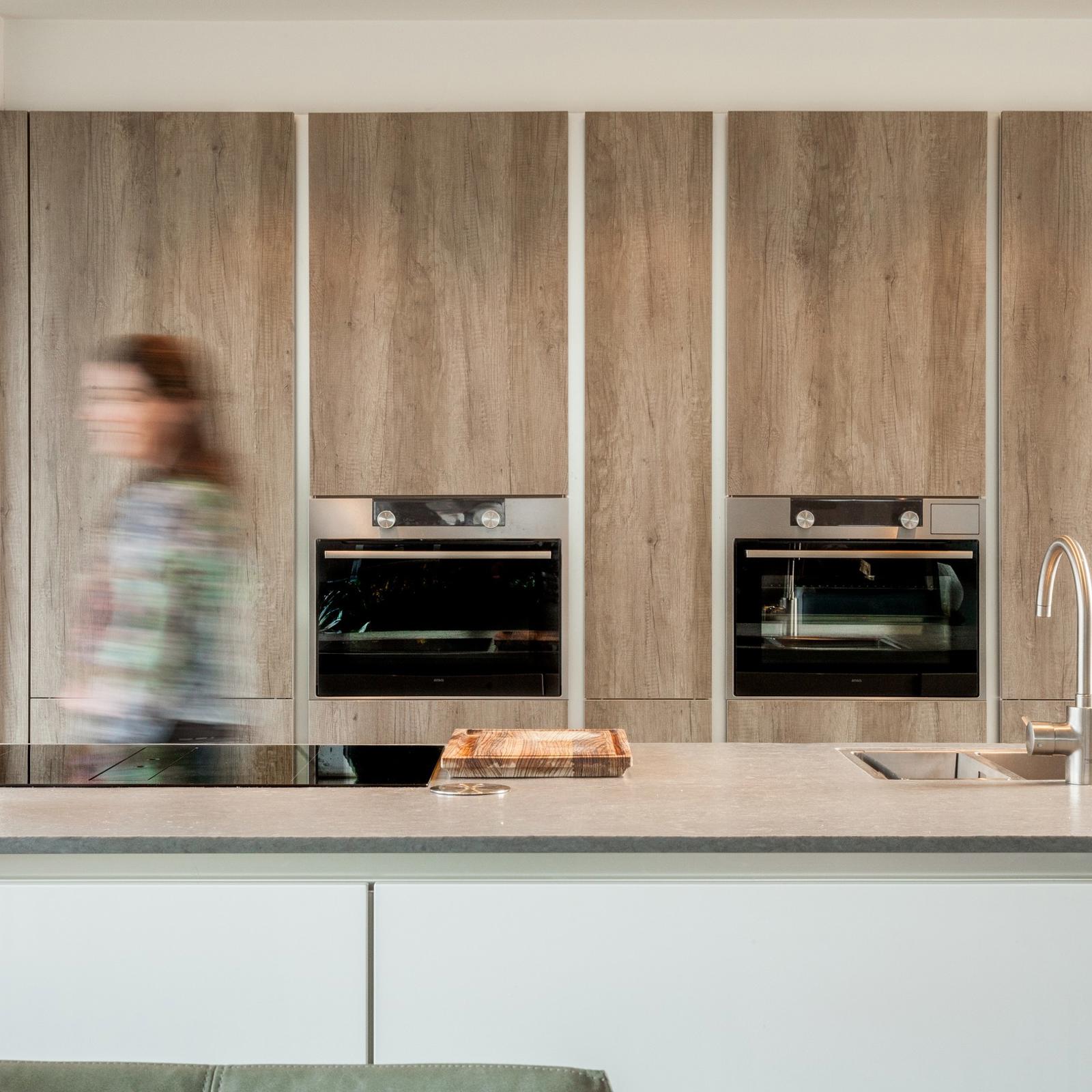 Houtlook keuken in Brunssum: kastenwand in houtlook met twee inbouwovens achter het kookeiland met spoelbak