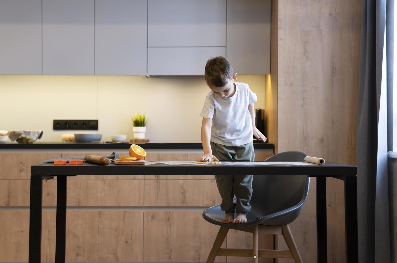 Jongetje staat op een stoel en reikt over de keukentafel in een keuken met houten fronten