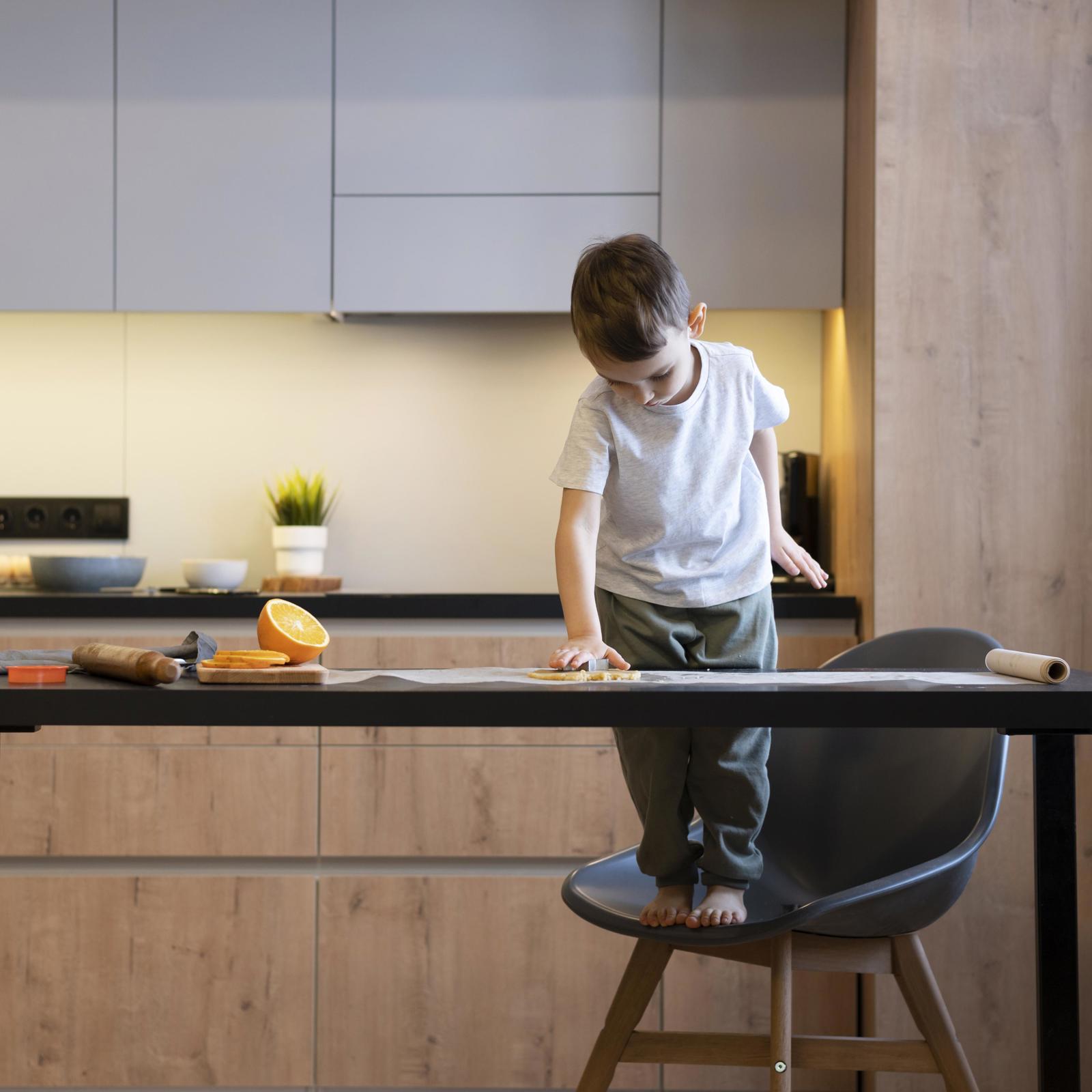 Jongetje staat op een stoel en reikt over de keukentafel in een keuken met houten fronten