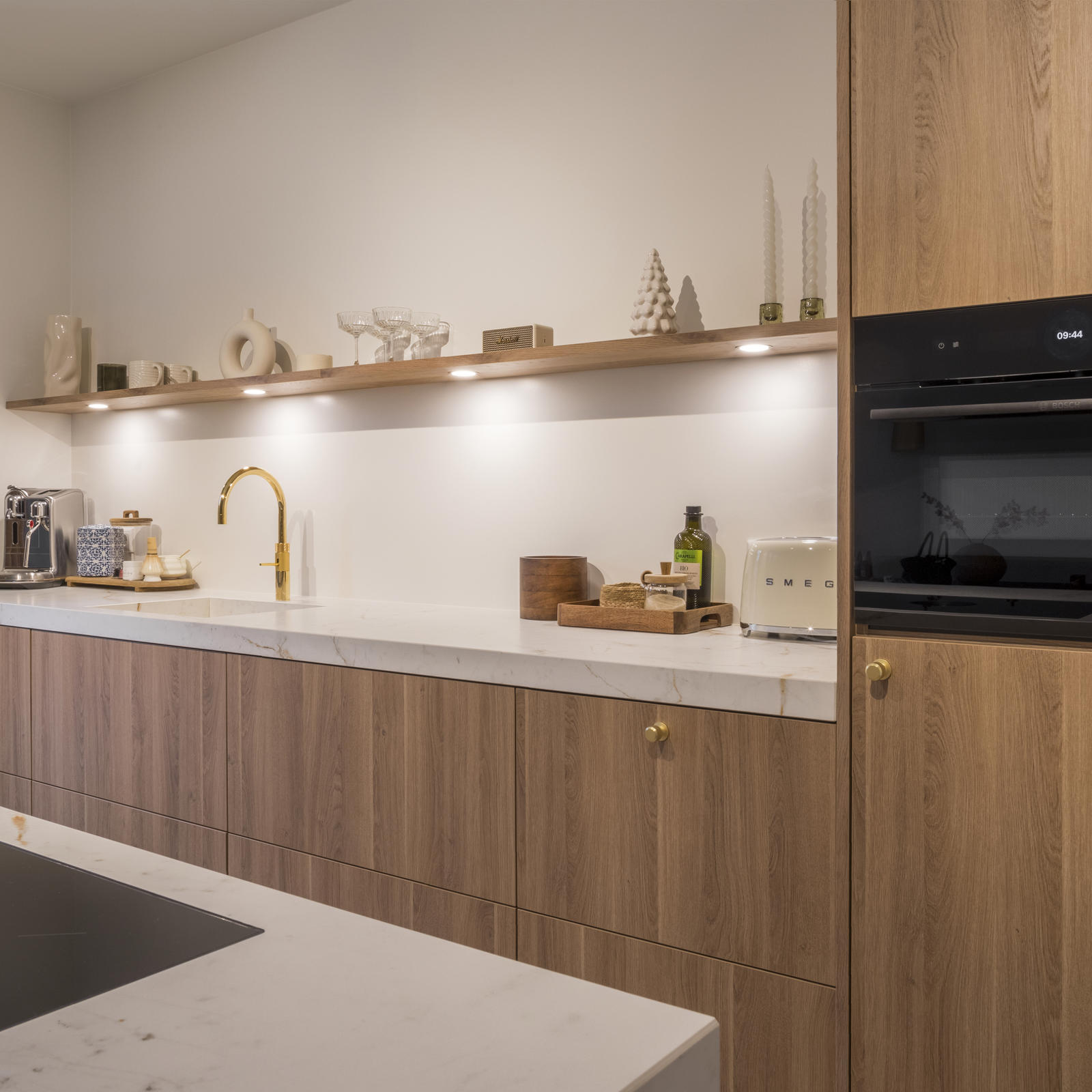 Keuken met eilandblad in brugvorm in Maastricht Oost: houten fronten, gouden kraan, zwevende plank en inbouwoven