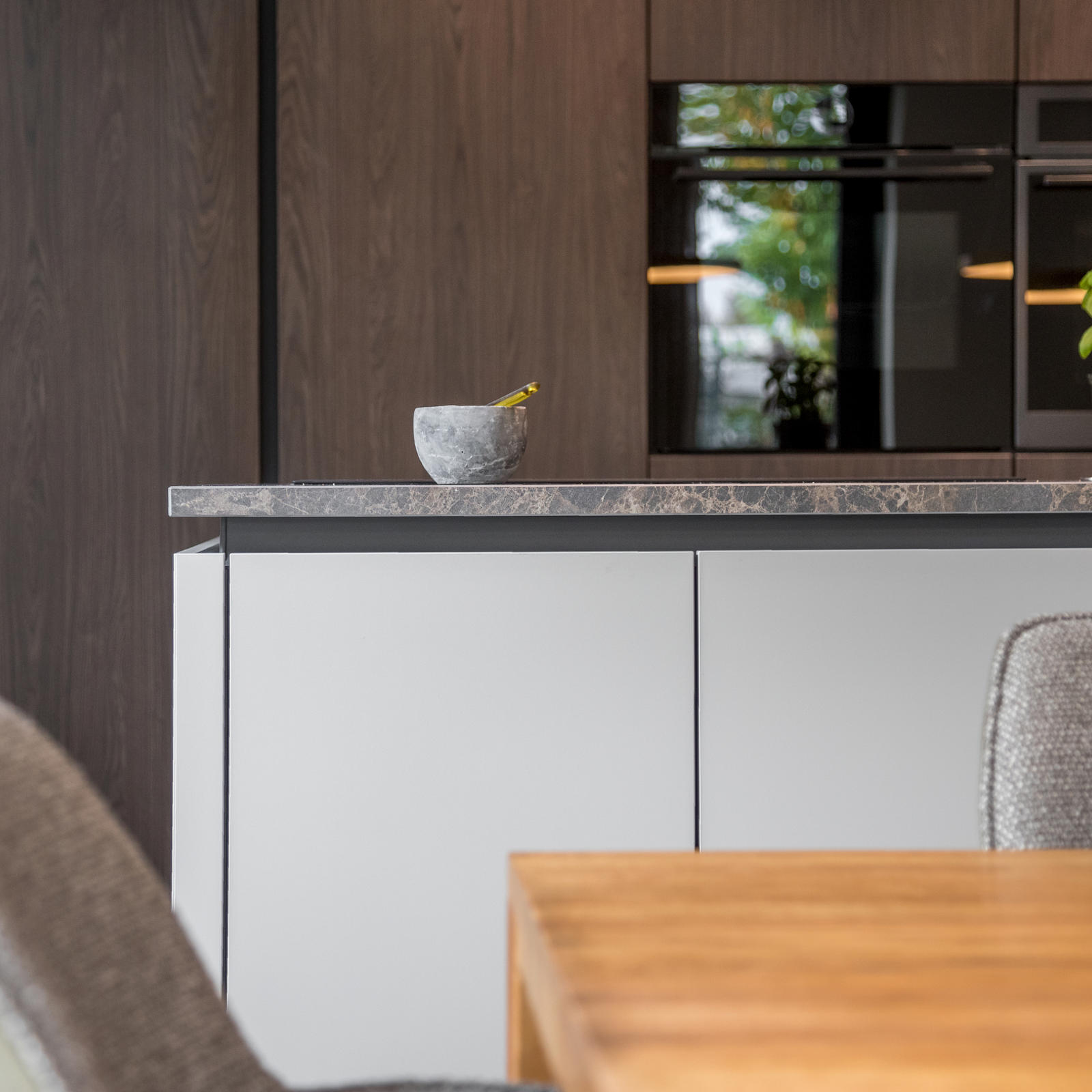 Witte greeploze onderkasten met marmerlook werkblad en inbouwovens in houtlook kasten