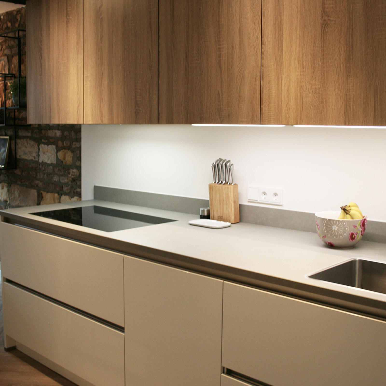 Maatwerk keuken in Maastricht: lichte onderkasten, houten bovenkasten en een natuurstenen muur