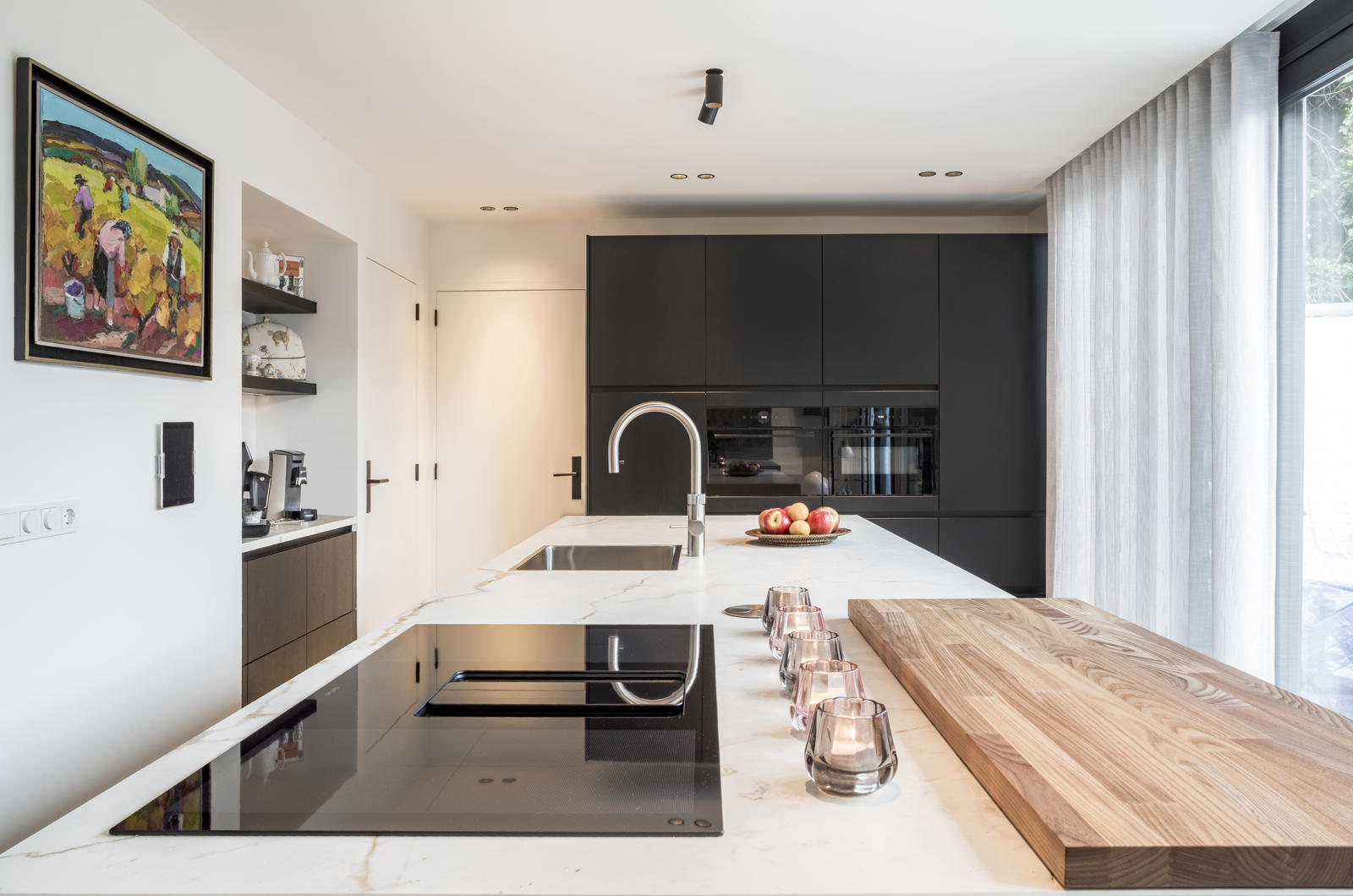 Strakke keuken met kookeiland in Maastricht Oost: keramisch werkblad, inductiekookplaat met downdraft en houten snijplank