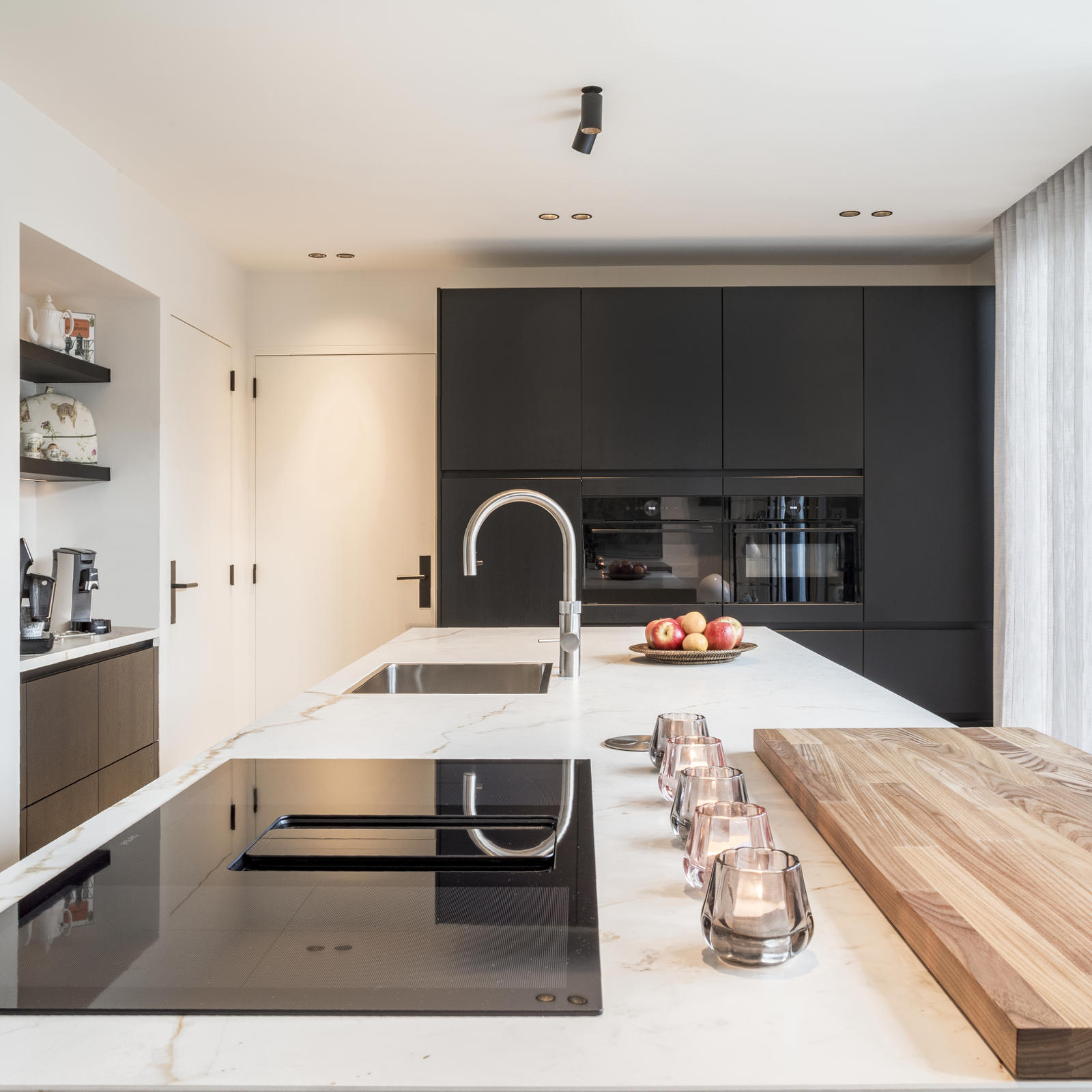 Strakke keuken met kookeiland in Maastricht Oost: keramisch werkblad, inductiekookplaat met downdraft en houten snijplank