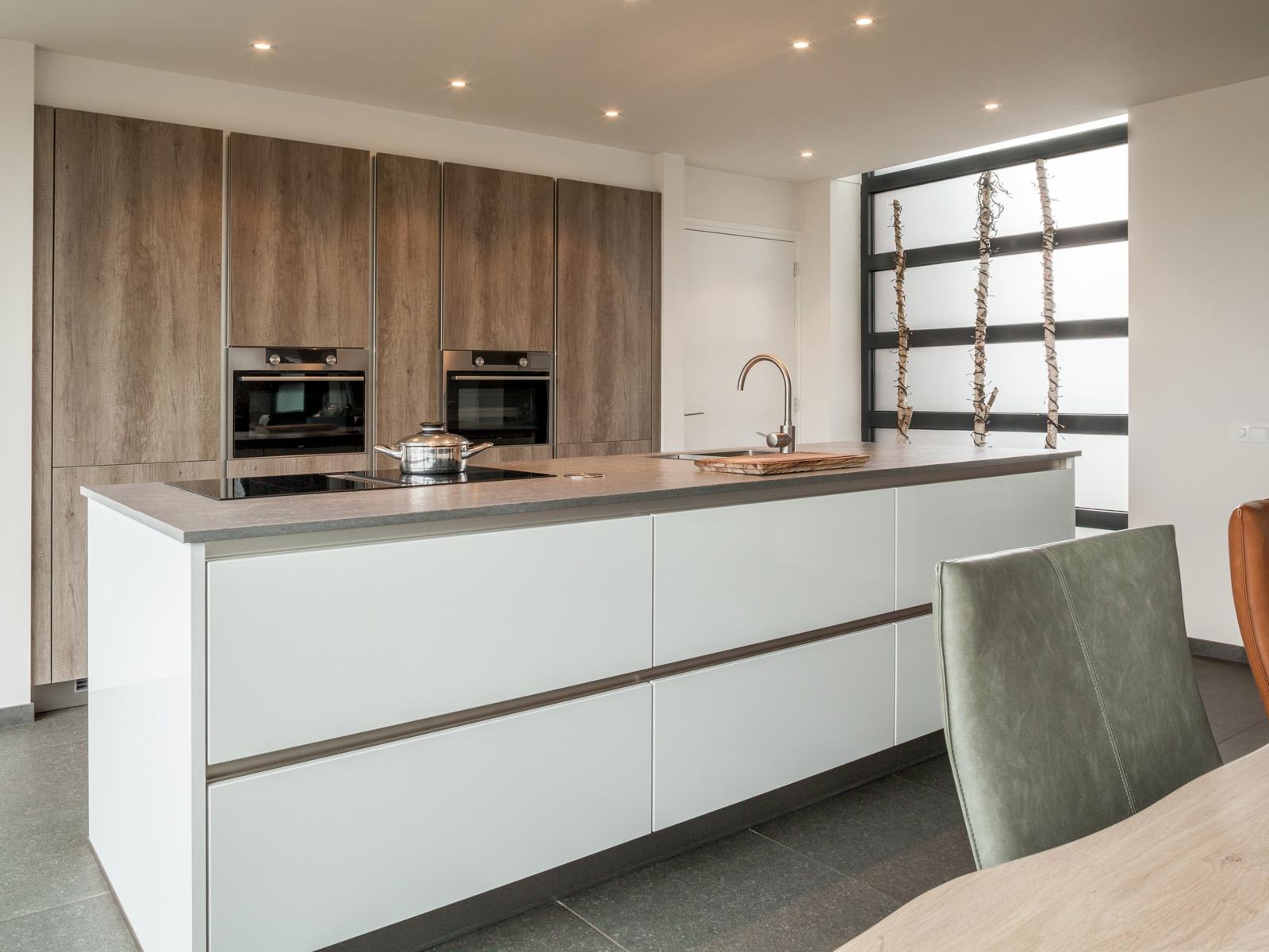 Houtlook keuken in Brunssum: wit kookeiland met inductiekookplaat en greeplijsten voor een houtlook kastenwand
