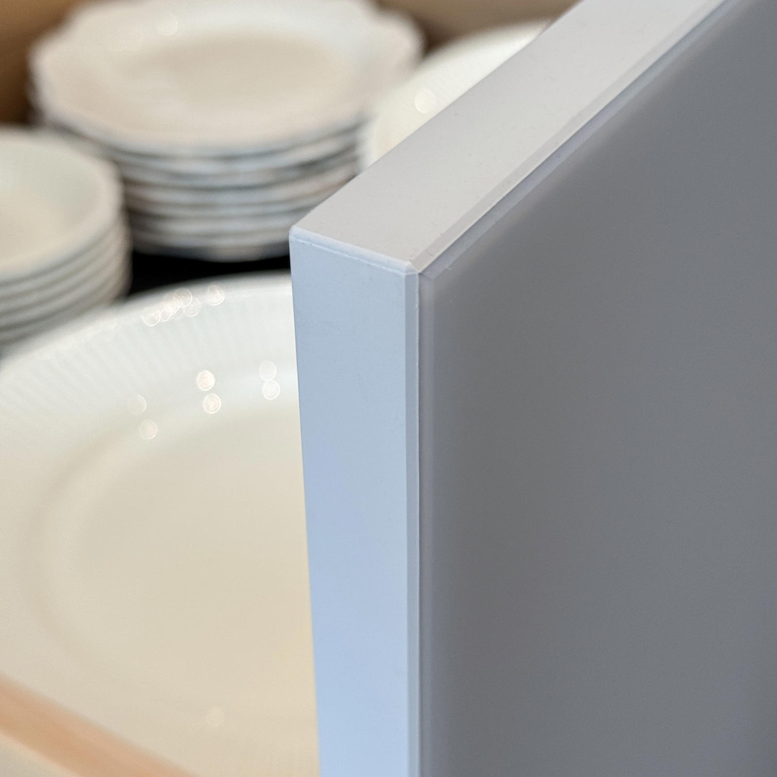 Detail van de afgewerkte rand van een lichtgrijs front, met servies in een lade erachter