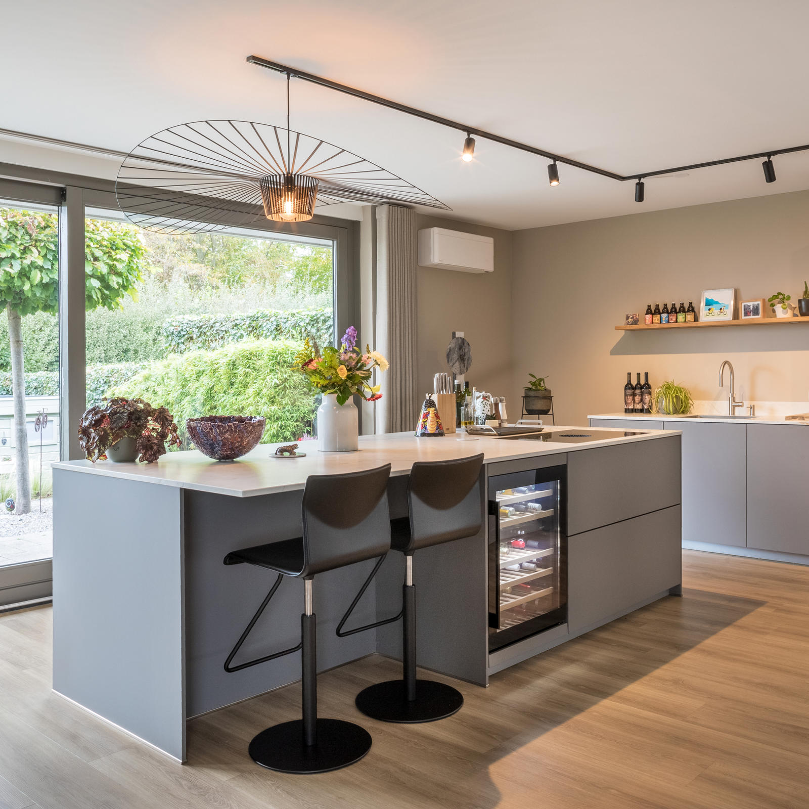 Keuken met kookeiland in Meerssen: taupe keuken met kookeiland, barkrukken, wijnklimaatkast en tuinzicht