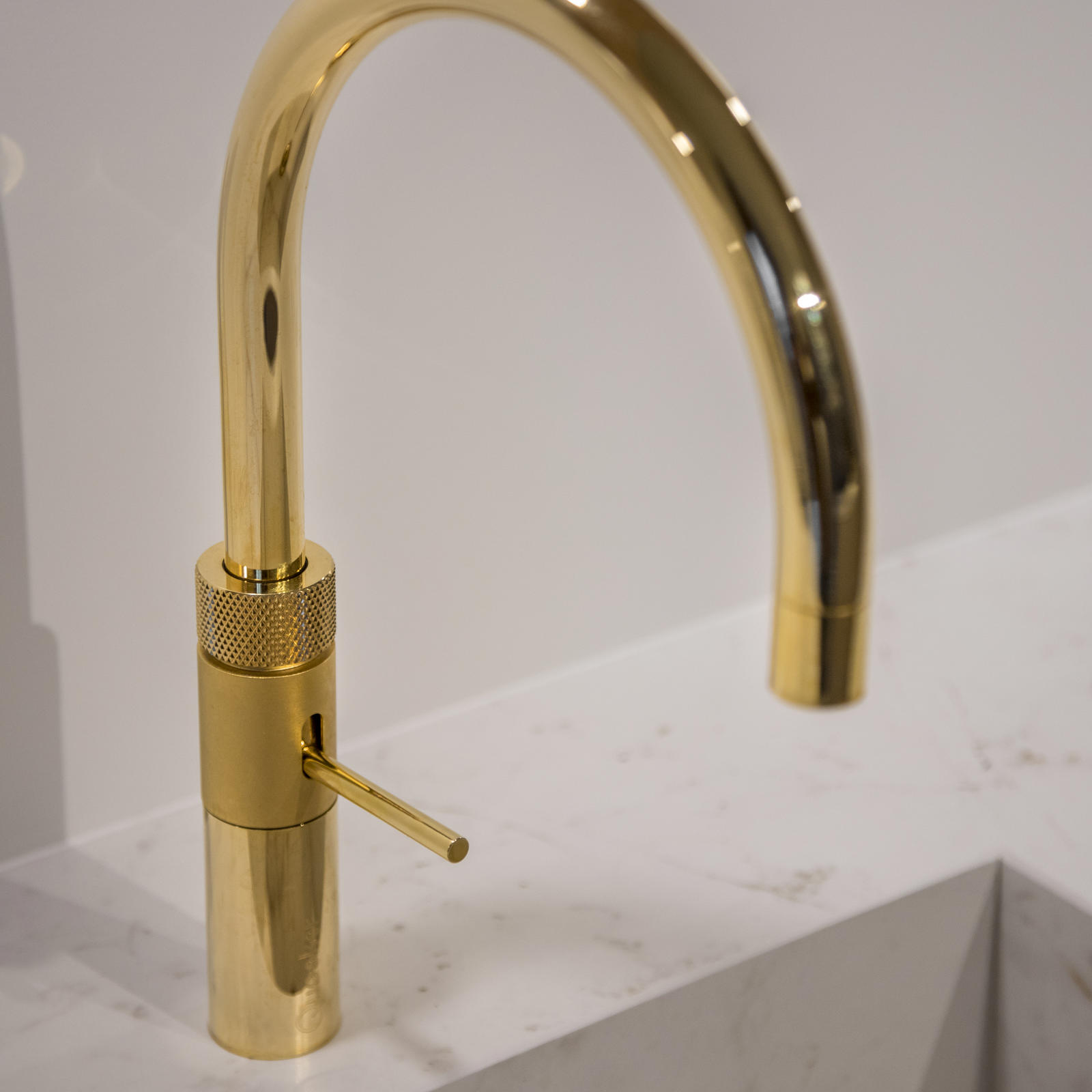 Goudkleurige kraan met booguitloop boven een spoelbak van wit marmerlook materiaal