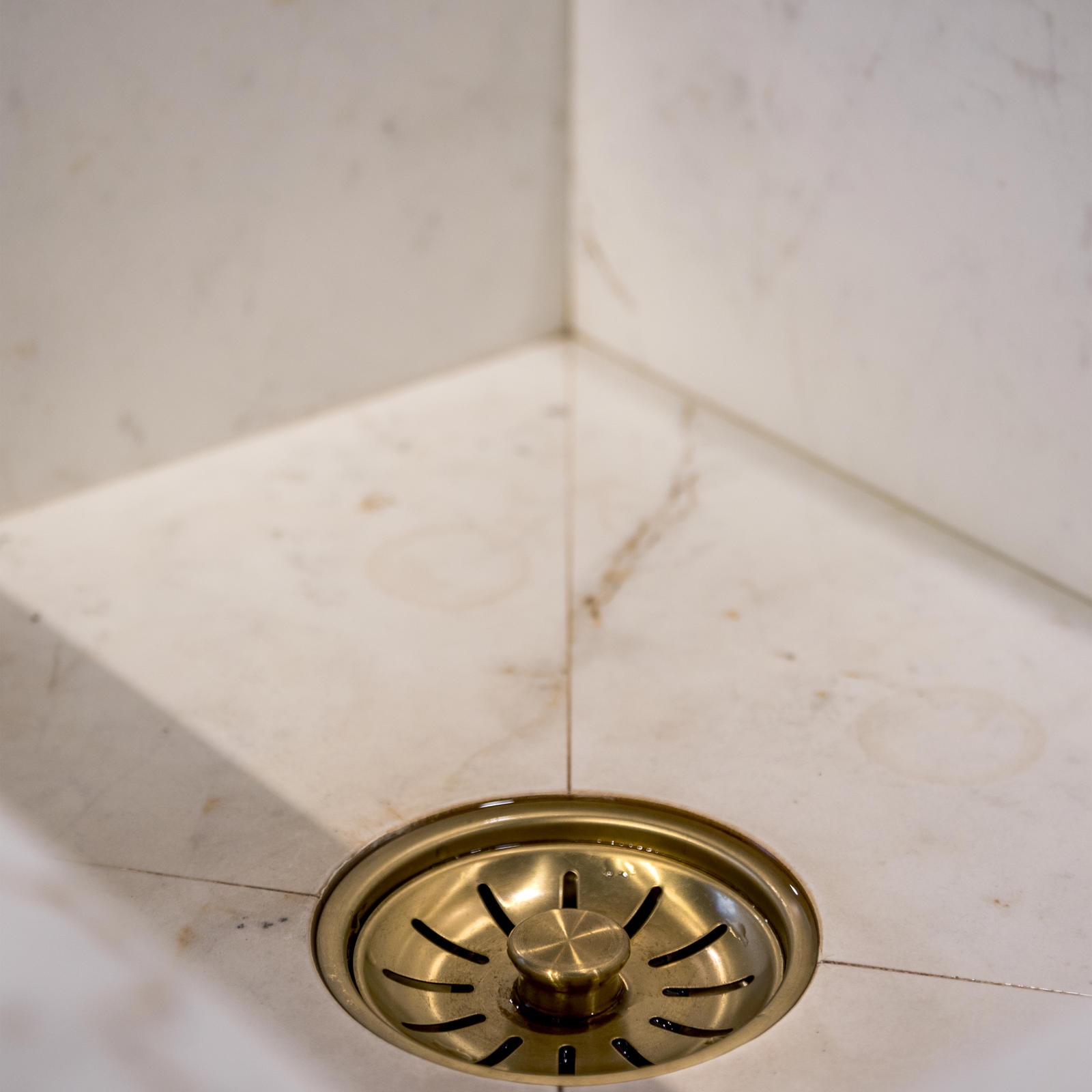 Spoelbak in wit marmerlook materiaal met goudkleurige afvoerplug
